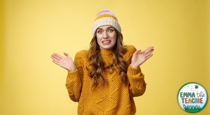 A person wearing a yellow knitted jumper and striped wooly hat has their hands up and an expression of guilt or apology for something.