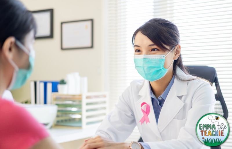 A doctor with a pink breast cancer ribbon on her jacket is talking to a patient in her office.