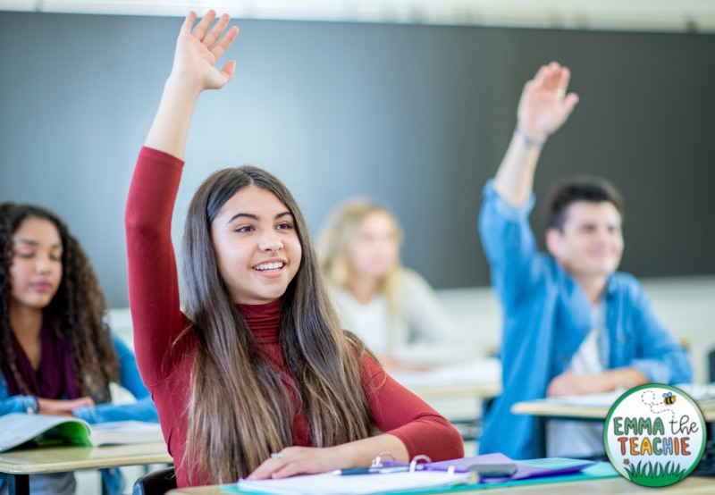 A classroom of students sitting in desks raising their hands to participate. Encouraging student participation is another way to build good relationships with students.