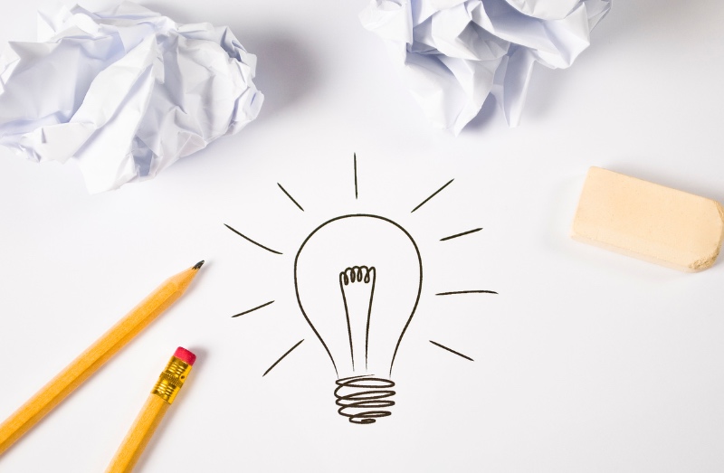 An image showing a drawn lightbulb, which indicates a good idea. There is crumpled paper, pencils, and an eraser surrounding the lightbulb.
