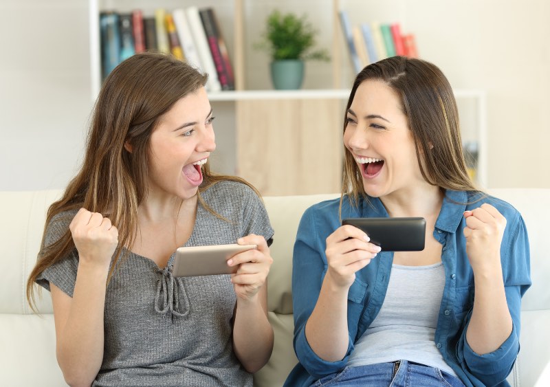 Two girls looking excited and holding their cell phones. Their forearms are in a fist, indicating something good has happened.