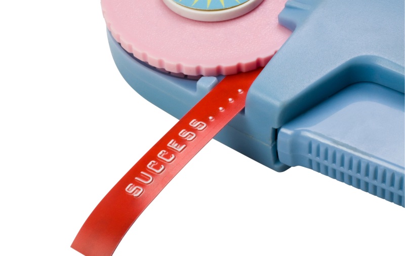 An image of a label maker printing out a red label. On the label, it reads, “SUCCESS.”