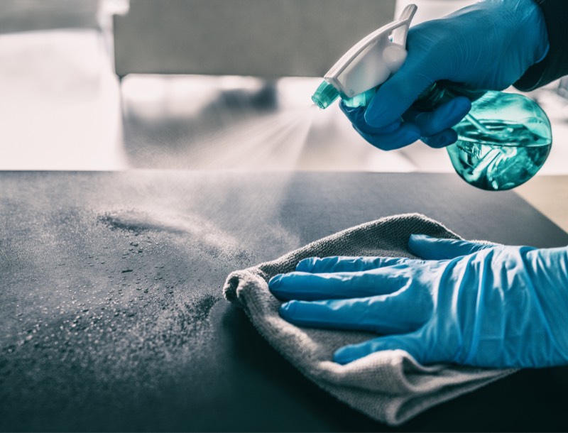 An image showing two hands wearing blue gloves sanitizing a lab table.
