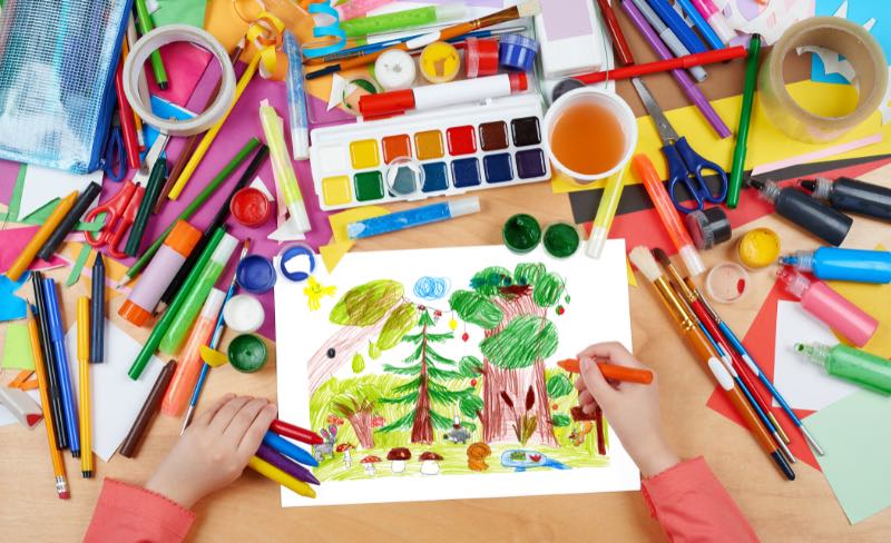 An image of two hands creating a wildlife painting. Markers, paintbrushes, paint, and other art supplies are scattered around the area. Creating art pieces is one of the suggested World Wildlife Day activities.