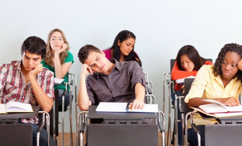 A classroom of bored students sitting at their desks with their heads in their hands.