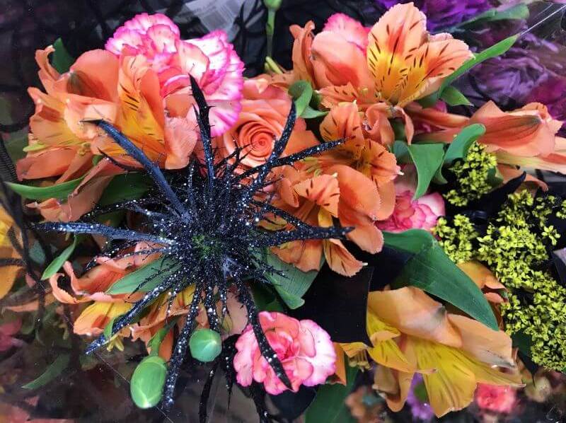 An image of a Halloween inspired flower bouquet. The flowers are purple, orange, pink, yellow, and black.