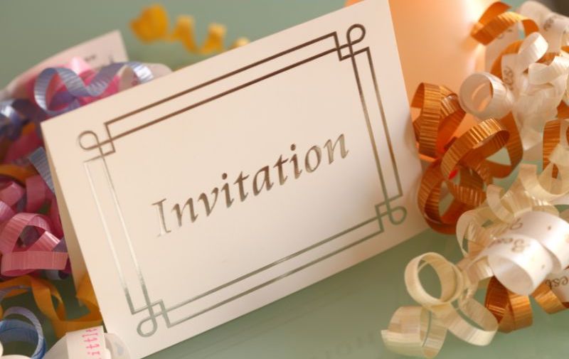 An image of a folded card invitation surrounded by ribbons of various colors.