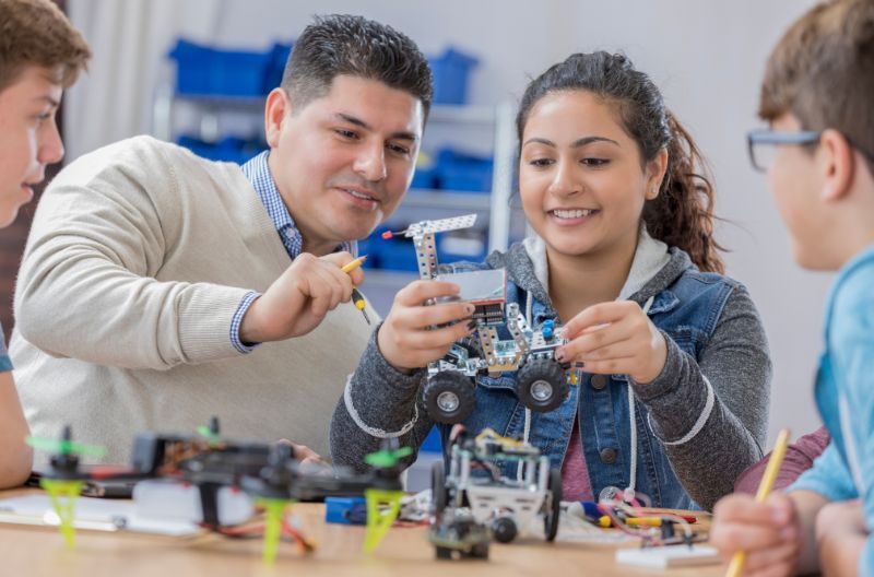 An image of 2 parents looking at a work sample of a robot that their student created.
