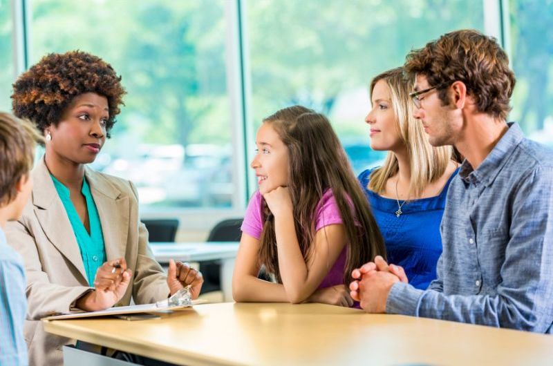 An image of a teacher sitting at a table with a student and her two parents.
